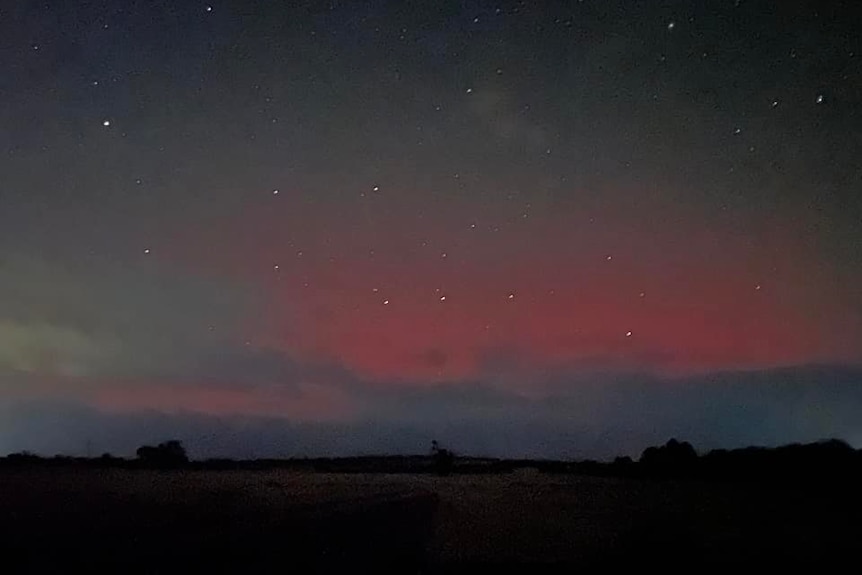 A dark paddock and sky with a red glow behind clouds. 