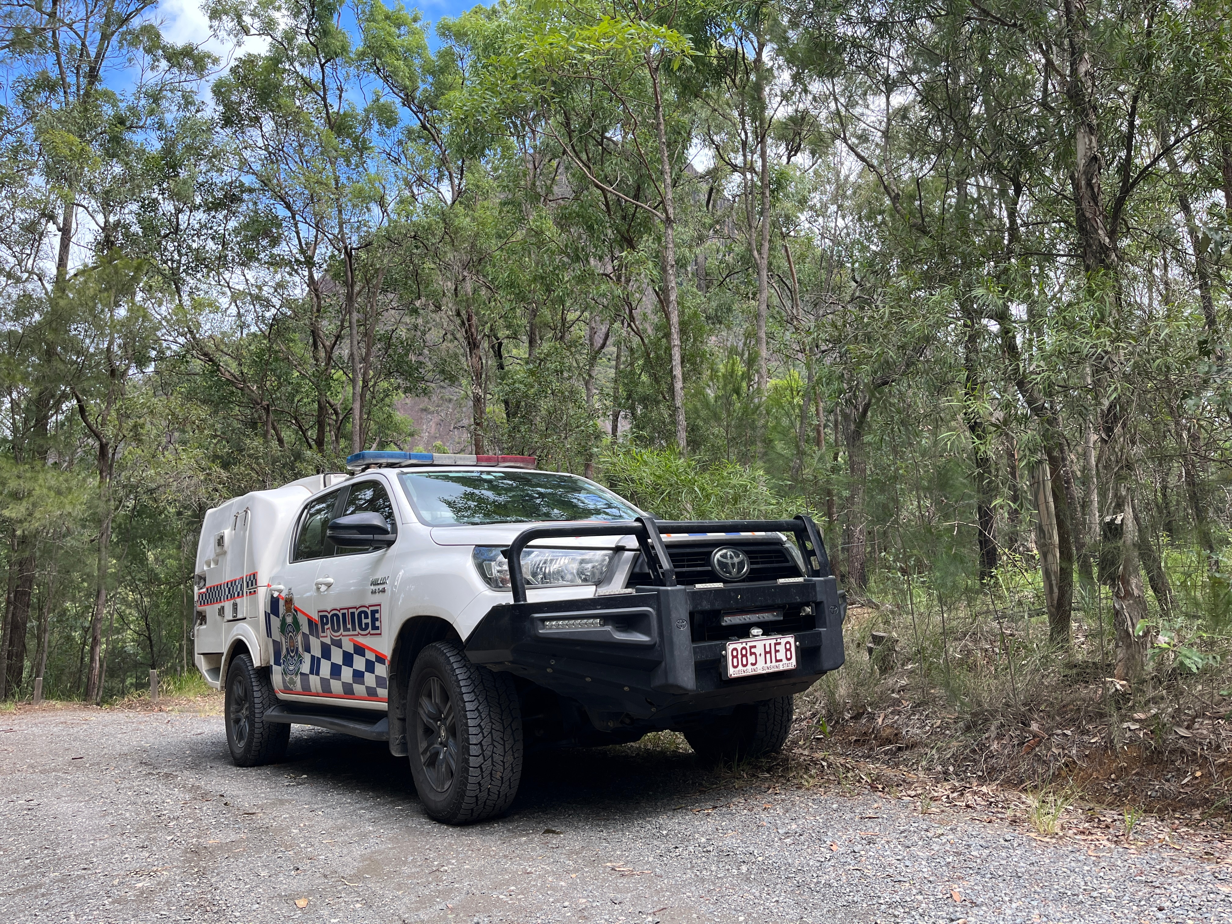 Police vehicle parked, bushland and mountain in the background.
