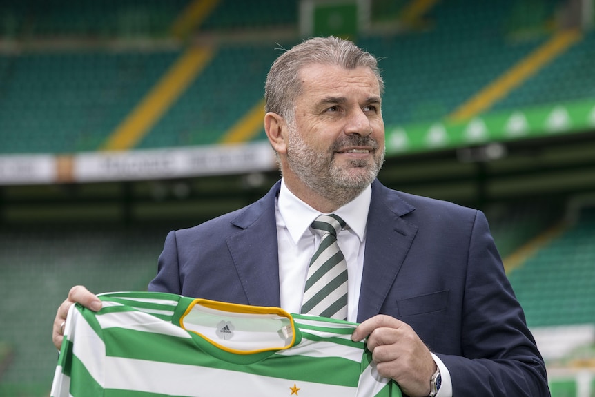 Ange Postecoglou holds a Celtic jersey and smiles