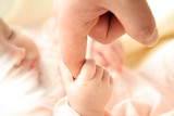 A baby holding an adult's finger.