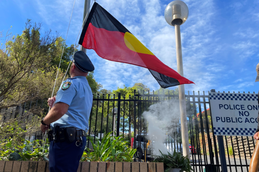A police officer looks up at Aboriginal flag as he raises it.