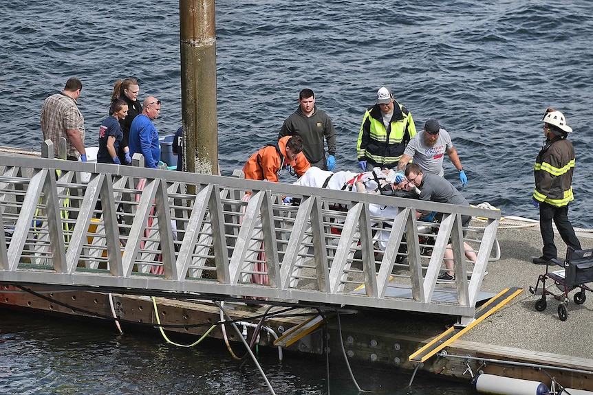 Emergency crews move a person on a stretcher towards a ramp on a seaside dock.