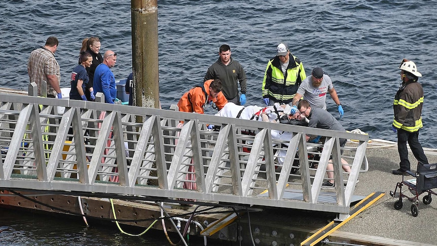Emergency crews move a person on a stretcher towards a ramp on a seaside dock.