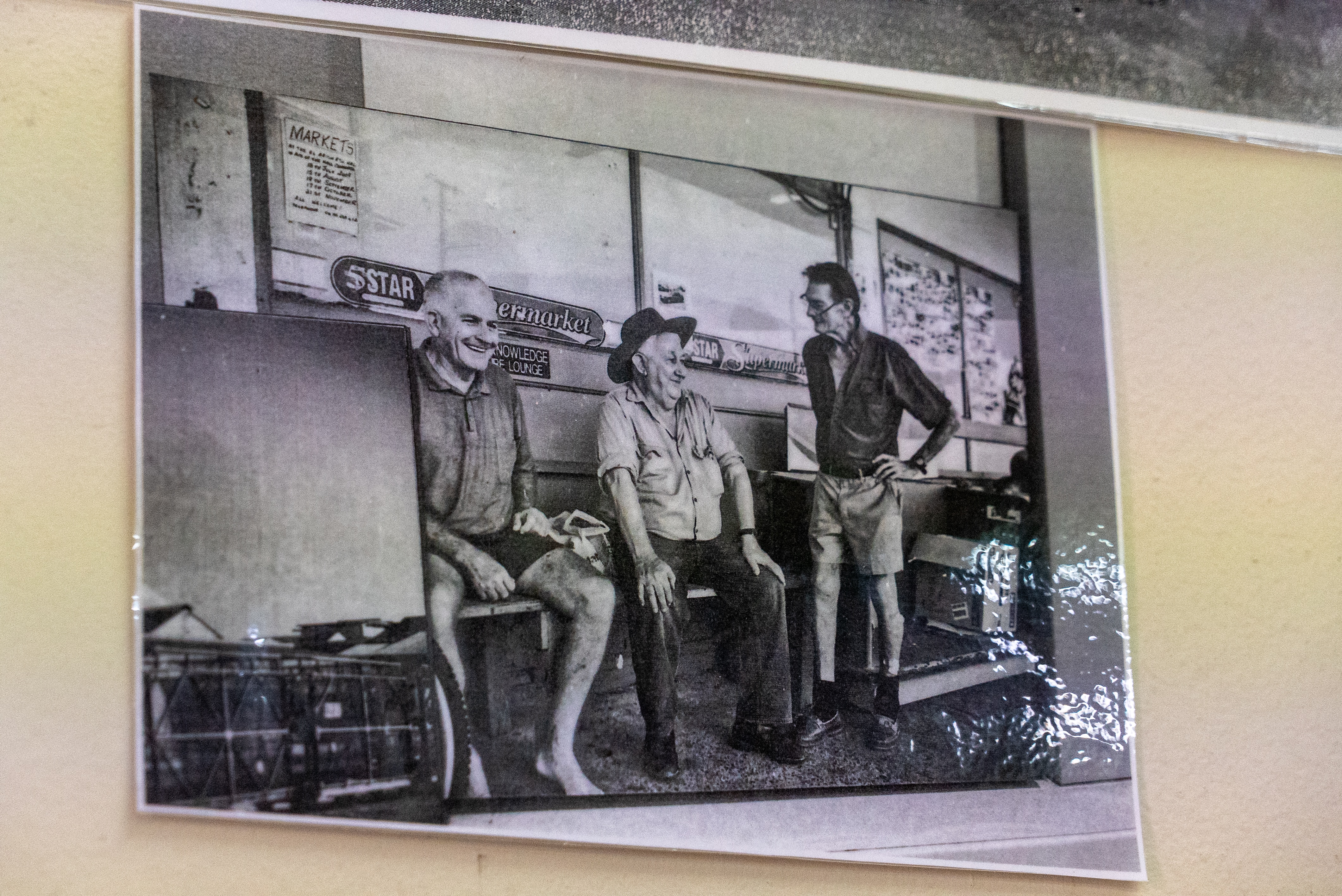 Una imagen en blanco y negro de tres hombres en un banco frente a un supermercado.