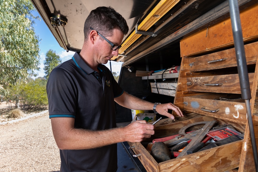 A middle-aged man reaches for tools in the back of his ute.