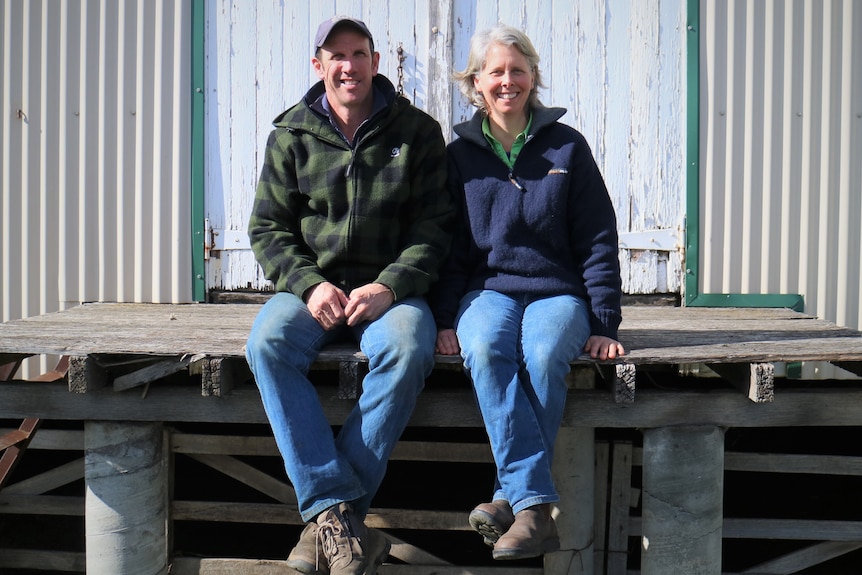 a man and a woman sit on some old timber floorboards at the back of a shed