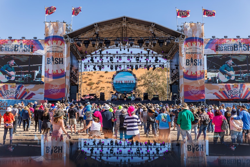 A crowd gathers at an outdoors stage at a music festival