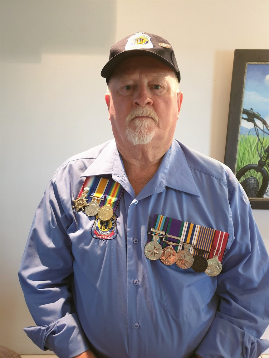 Bob is wearing a blue shirt with his war medals on on side and his father's medals on the other side of his chest.