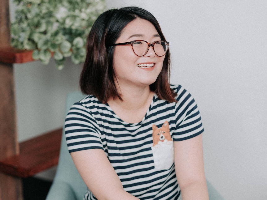 Therapist Michelle Lin, smiles on a blue chair, wearing a striped shirt with a cartoon dog on it.
