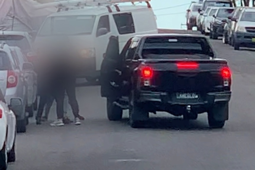 Men blurred stand next to black SUV