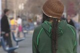 A dreadlocked youth in a beanie faces away from the camera.