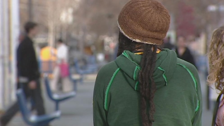 A dreadlocked youth in a beanie faces away from the camera.