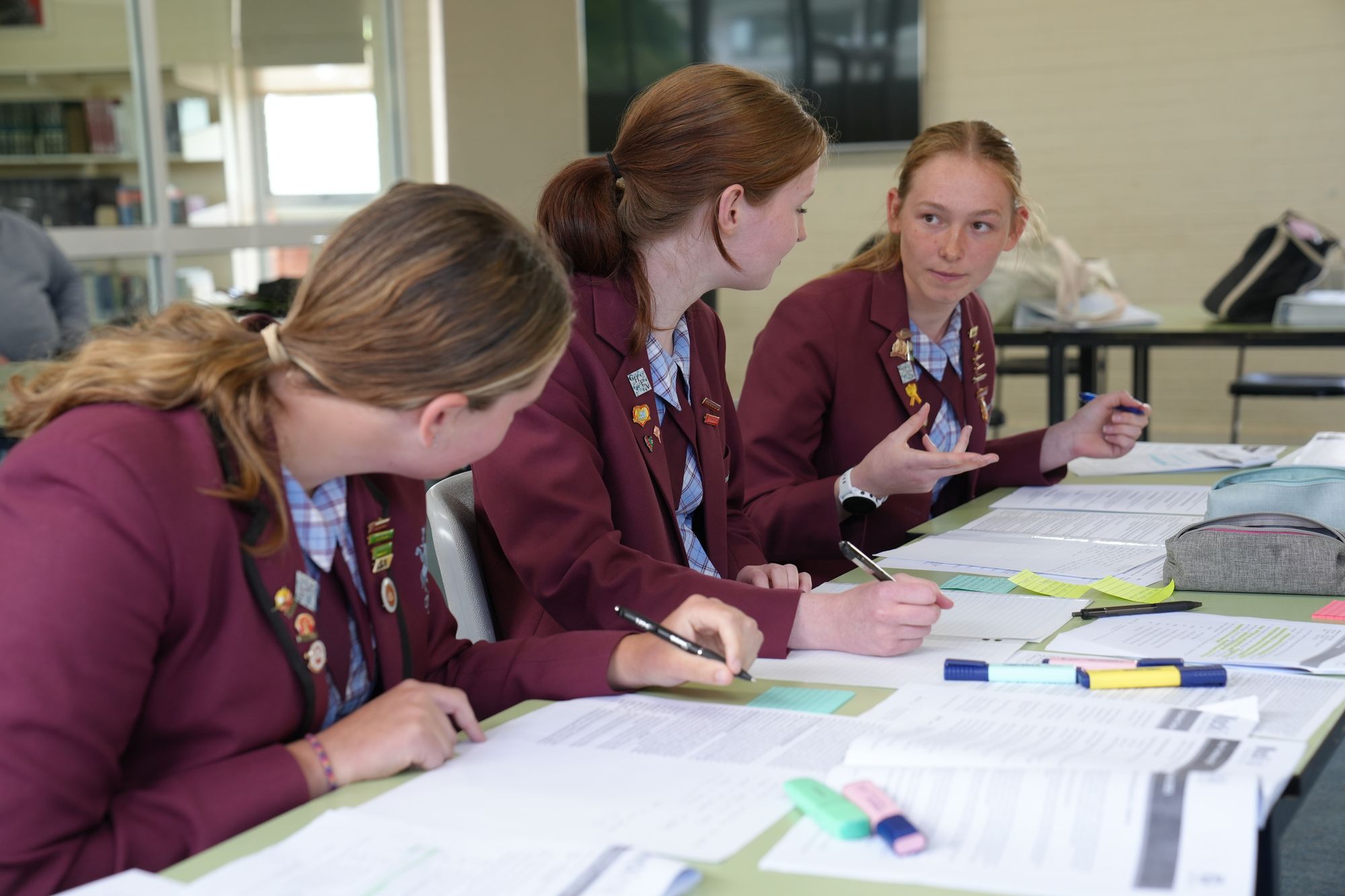 Three students in maroon blazers sitting in classroom desk