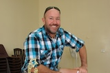 A bald man with sunglasses on his head, wearing a flannel shirt and smiling broadly.