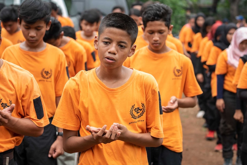 Young men in orange 'Hard Liners' shirts stand in rows.