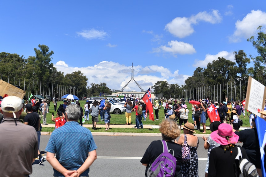 A crowd of people with Australian flags old signs against COVID-19 vaccinations.