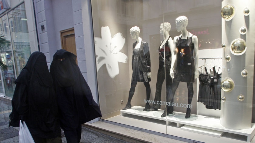 Women wearing niqabs walk past clothing stores in France.
