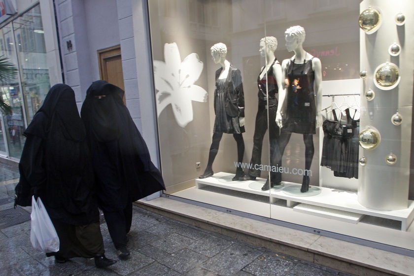 Women wearing niqabs walk past clothing stores in France