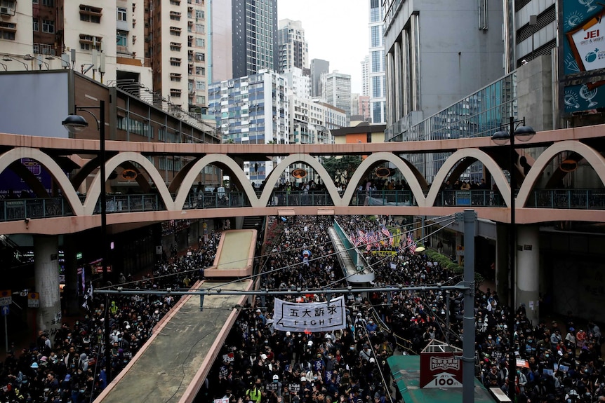 A view of a bridge above a street flooded with people marching and skyrises in the background, banner reads "fight".