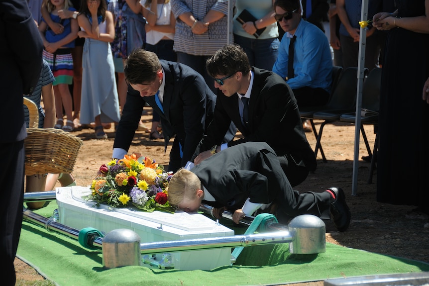 Family over a coffin about to be lowered into the ground.