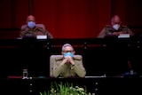 raul castro sits with his hands clasped wearing a mask