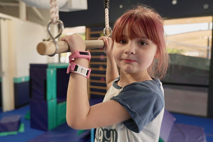 Ava stands at a bar in a gym.