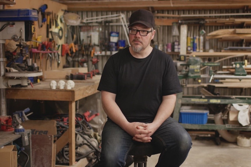 Jud Wimhurst sitting on a stool in a workshop with tools and equipment behind him