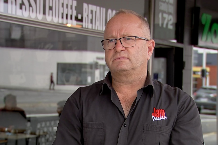 Man in black shirt and glasses standing outside a cafe. 
