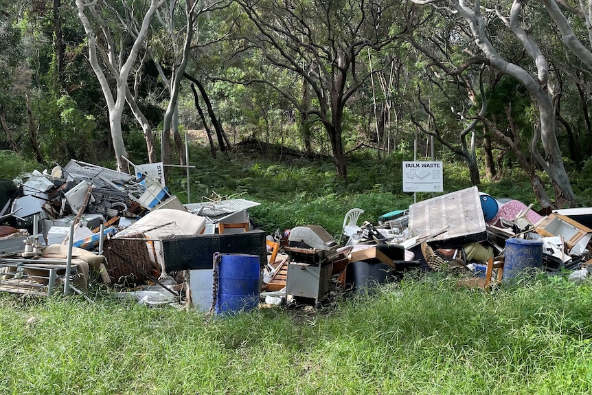 Assorted waste at a landfill in a green forest area, with a sign saying bulk waste.