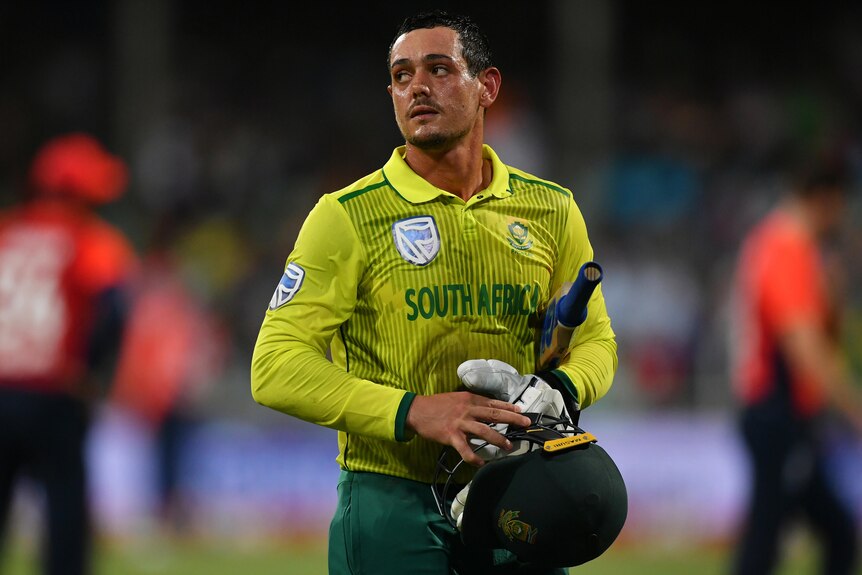 A South African male batter looks to his right as he walks off the field.