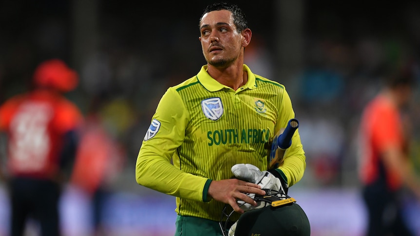 A South African male batter looks to his right as he walks off the field.