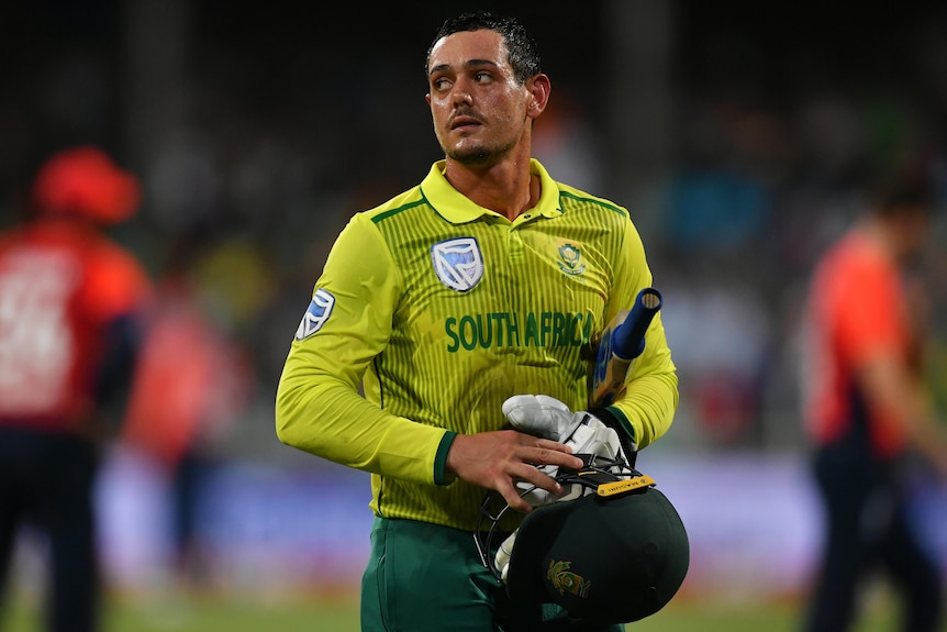 A South African male batter looks to his right as he walks off the field.