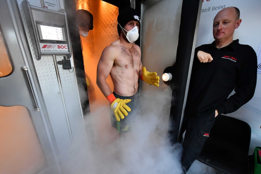 A man emerges from a cryotherapy chamber, wearing large gloves.