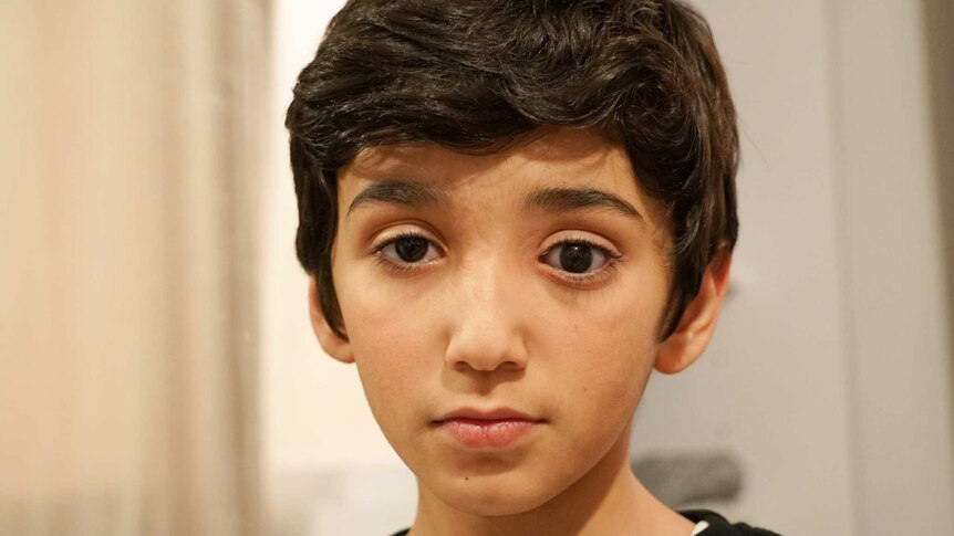 A boy with dark eyes and hair stares at the camera.