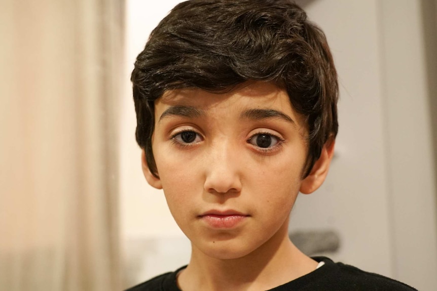 A boy with dark eyes and hair stares at the camera.