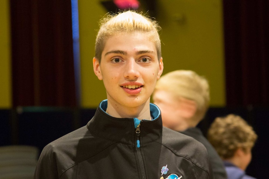 A young man looks at the camera, smiling.