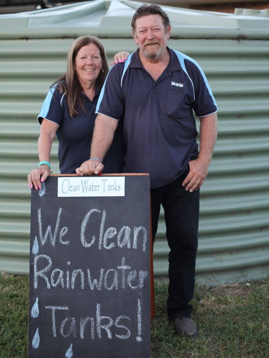 A man and woman stand with a sign that reads "we clean rainwater tanks"
