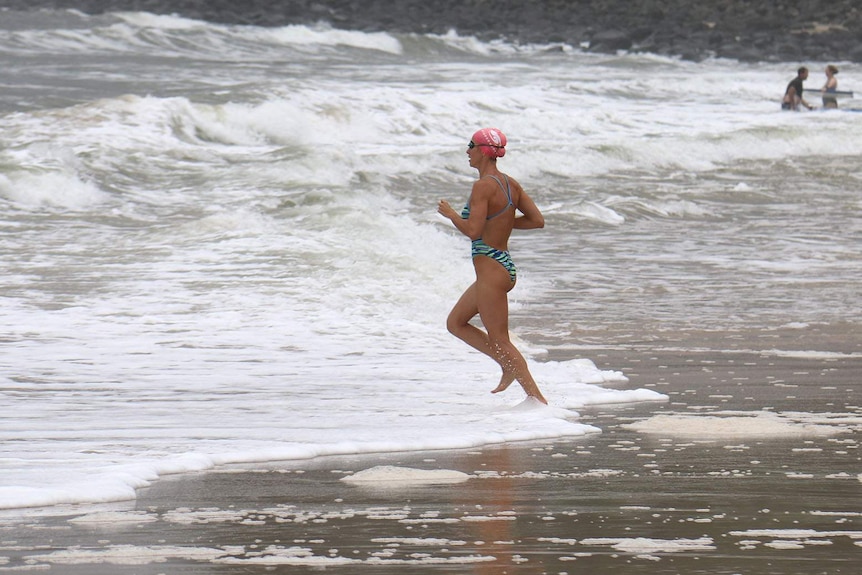 A woman swimmer runs into the water at the beach