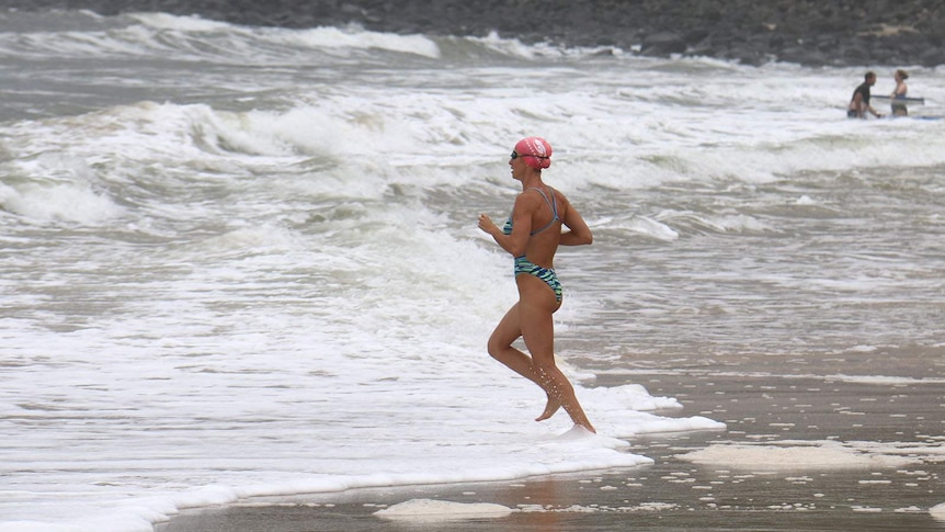 A woman swimmer runs into the water at the beach