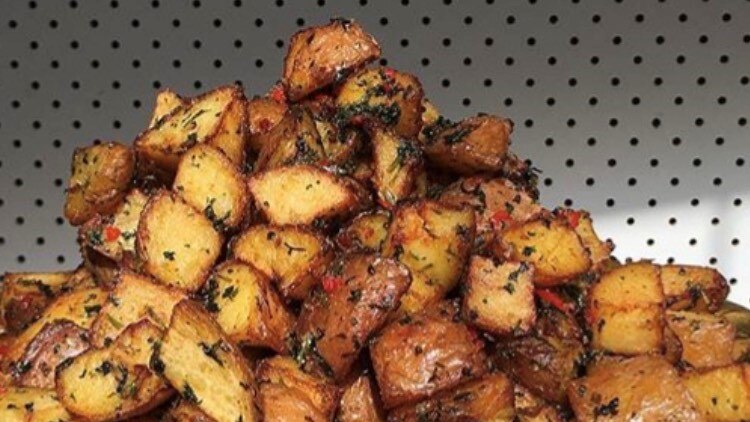 A hand holds a gold dish of spiced, roasted potatoes piled high.