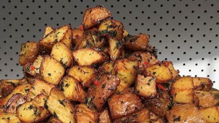 A hand holds a gold dish of spiced, roasted potatoes piled high.