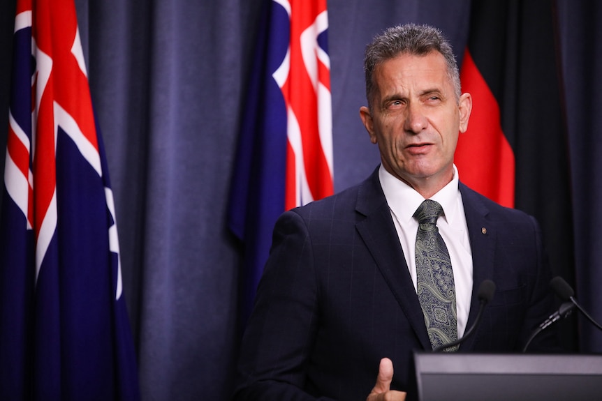 A mid-shot of WA Police Minister Paul Papalia speaking at a media conference indoors, wearing a suit and tie at a podium.