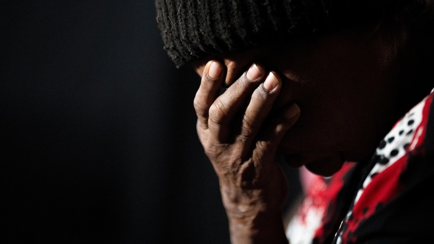 A person with dark skin wearing a beanie with their head resting in a their hand. 