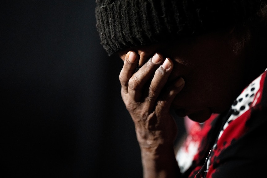 A person with dark skin wearing a beanie with their head resting in a their hand. 