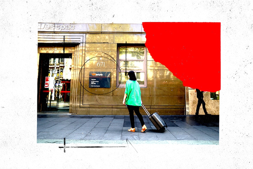 A woman walks towards the bank with a suitcase.