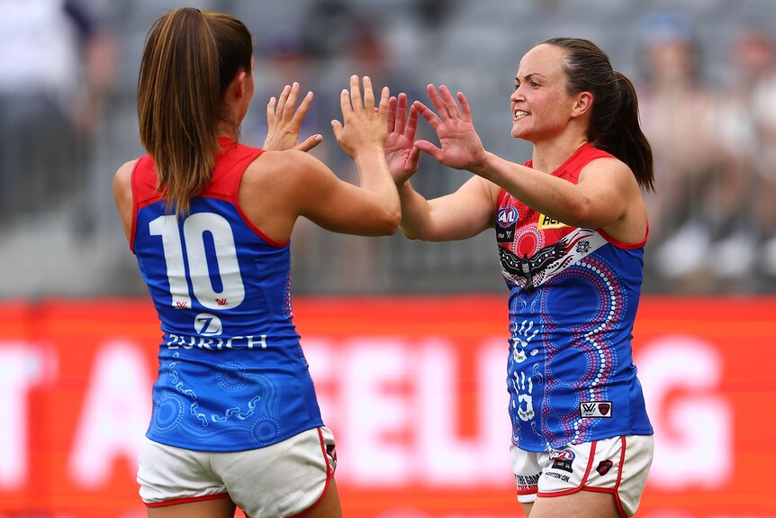 Two Melbourne AFLW players celebrate a goal.