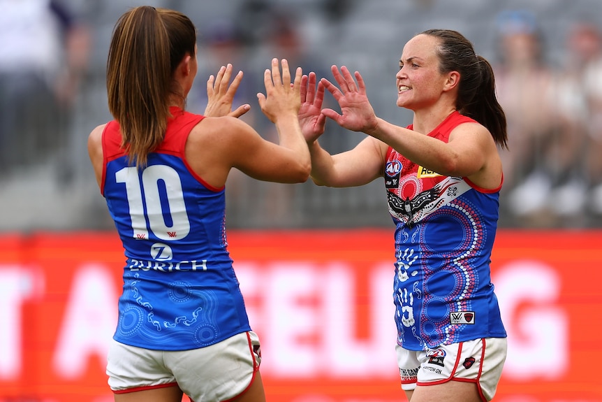 Two Melbourne AFLW players celebrate a goal.