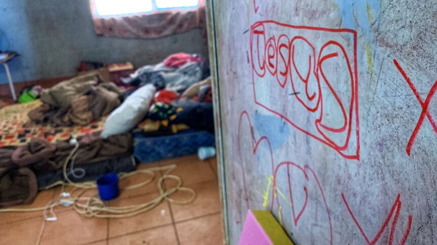 Inside a house with writing on the wall and a mattress on the floor.