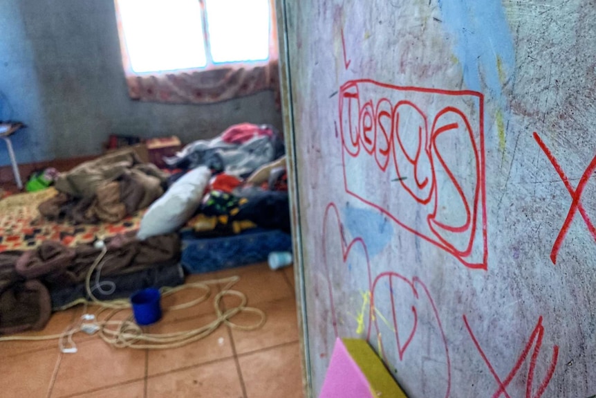 Inside a house with writing on the wall and a mattress on the floor.