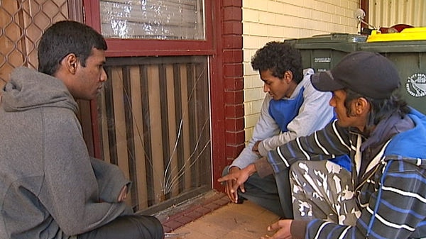 Three Sri Lankan stidents gather around a broken window at their Canberra home